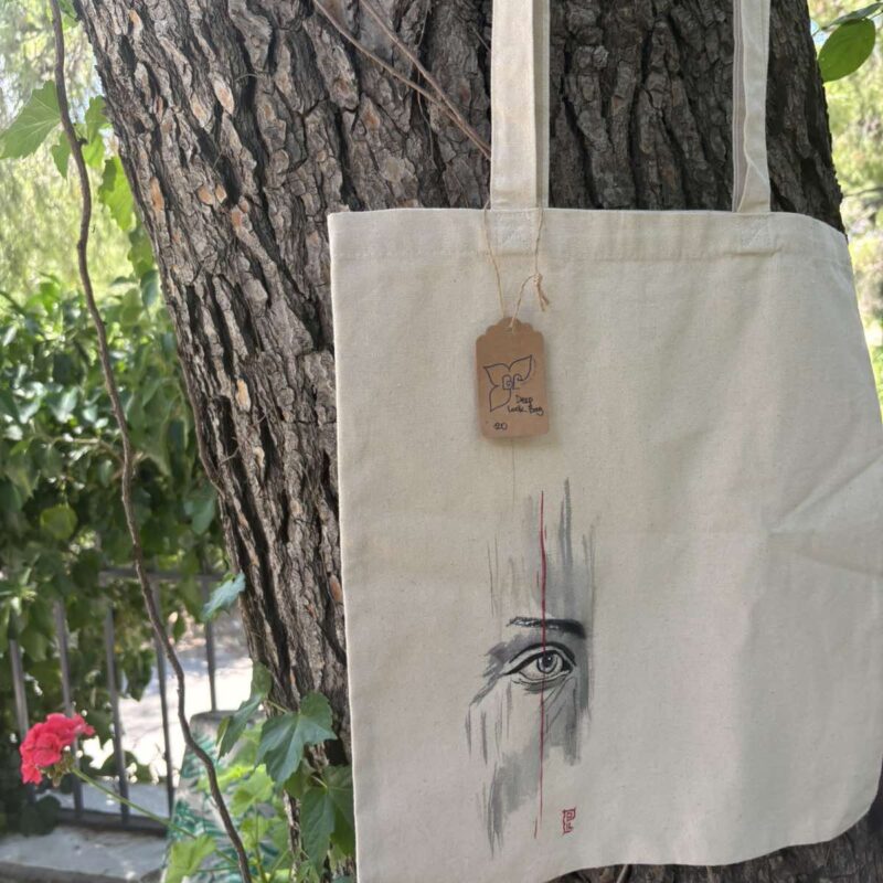 Hand-painted beige canvas tote bag featuring a minimalist expressive eye with black brushstrokes inspired by Japanese ink art.